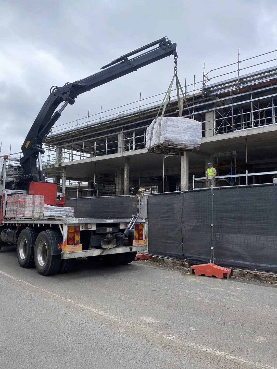 A truck mounted crane lifting a pallet of building materials onto a commercial construction site