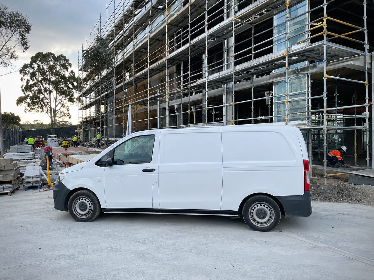 A Tradiez van parked beside a multi storey commercial building under construction with scaffolding