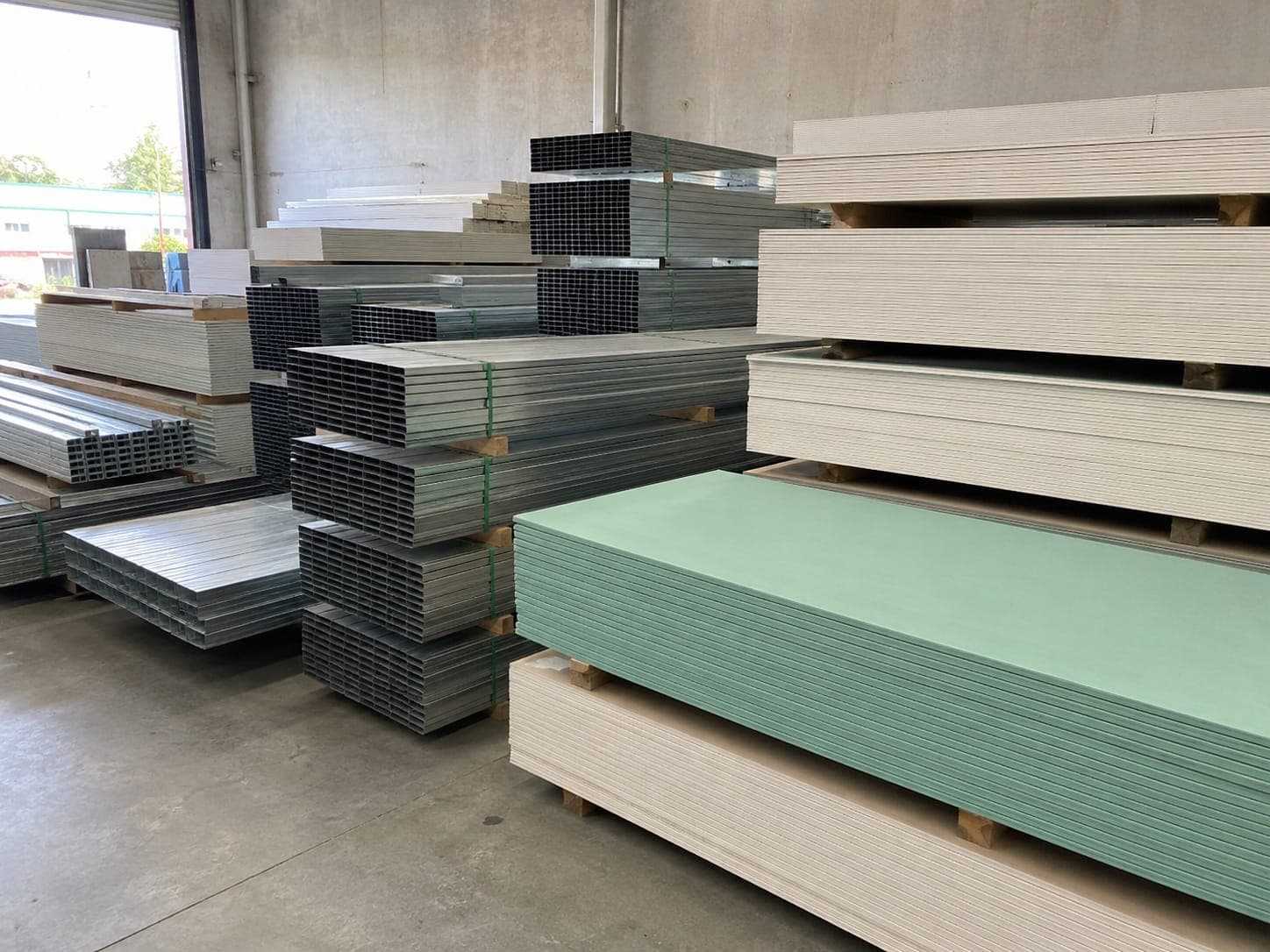 Neatly stacked plasterboard sheets and bundles of galvanised steel studs in a warehouse